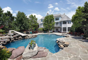 beautiful pool with stonework around it and white luxury house